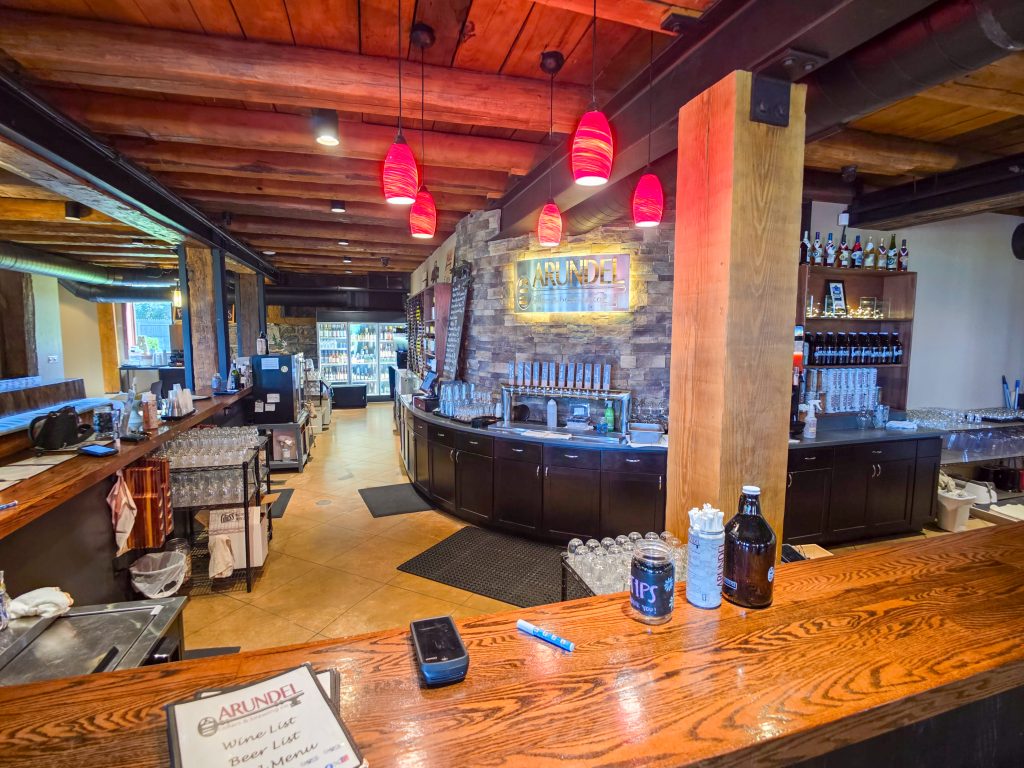 Wine and beer tasting room inside Arundel Cellars & Brewing with guests enjoying food and drinks.