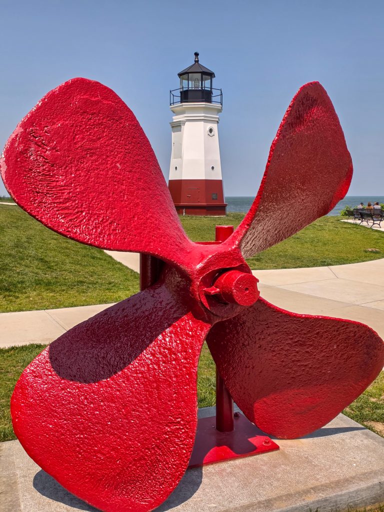 Vermilion Lighthouse seen through large ship propeller sculpture on Lake Erie shore